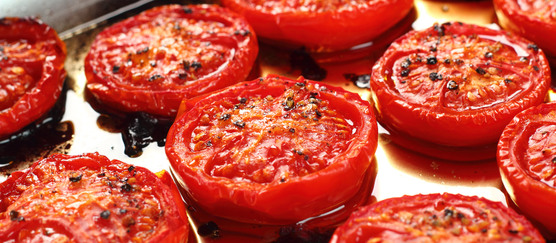 Geroosterde tomaten in een ovenschaal met kruiden en specerijen.