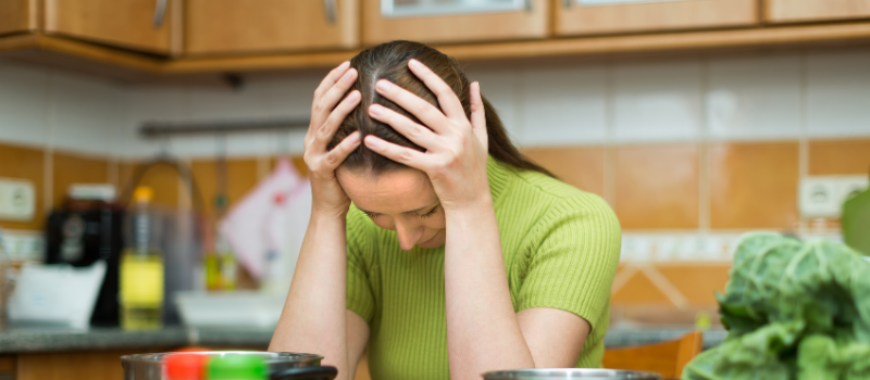 Gestreste vrouw in de keuken met groenten en gezond eten om haar heen.