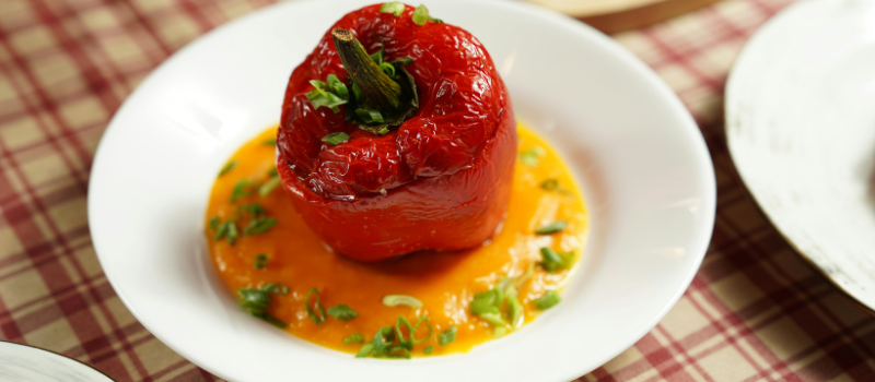 Geroosterde rode paprika geserveerd op saus met kruiden op wit bord