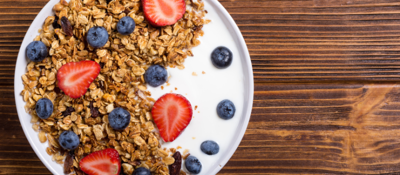 Kom met granola, yoghurt en vers fruit op houten tafel.