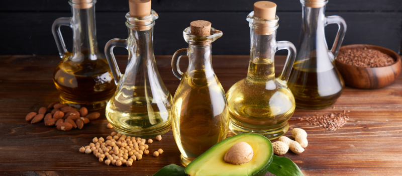 Diverse oliën in glazen flessen met avocado, soja en noten op houten tafel