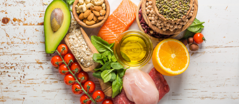 Diverse gezonde voedingsmiddelen zoals zalm, avocado, noten, en groenten in een hartvorm gerangschikt.