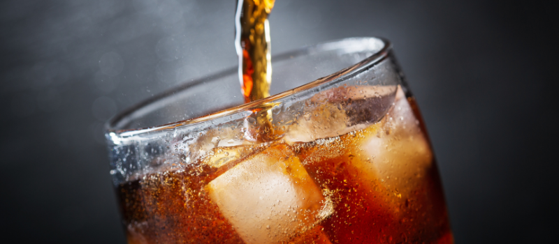 Donkere frisdrank wordt geschonken in glas met ijsblokjes
