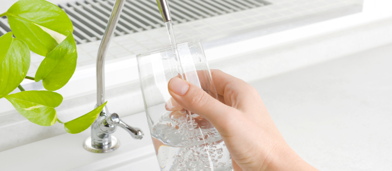 Hand vult glas met kraanwater bij moderne gootsteen
