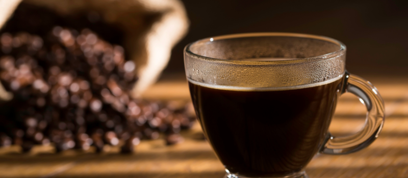 Glas zwarte koffie met koffiebonen op een houten tafel.