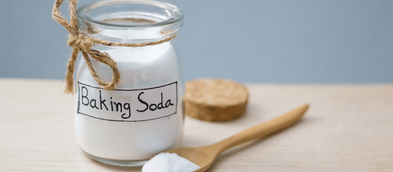 Een glazen pot met baking soda en een houten lepel op een tafel.