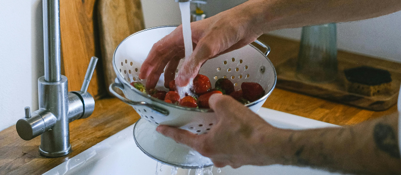 Hand spoelt aardbeien in vergiet onder kraan, schoon gezond fruit
