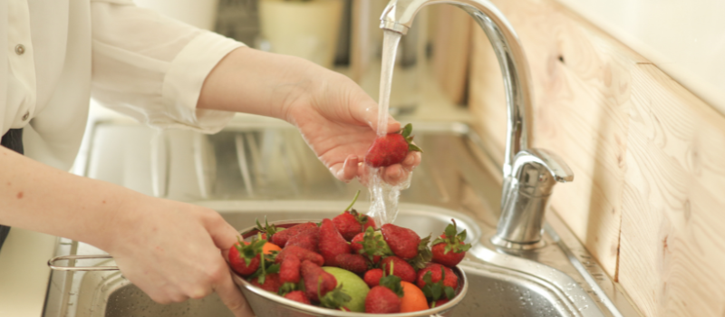 Hand wast verse aardbeien onder keukenkraan, gezond fruit