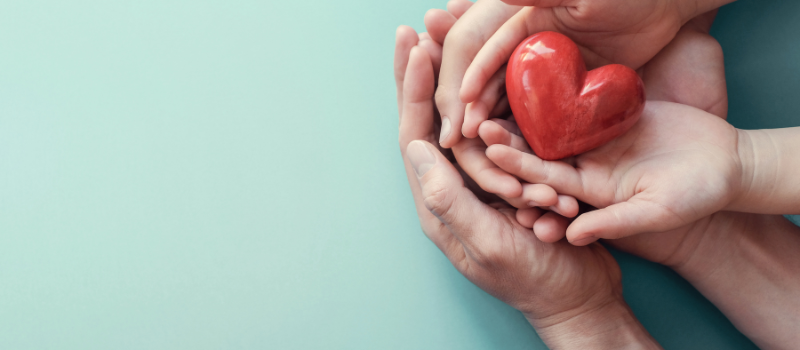 Volwassen en kinderhanden houden samen een rood hart, symbool voor zorg