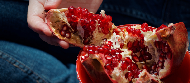 Handen scheuren gehalveerde granaatappel boven kom met pitten, vers gezond fruit