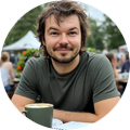 Portretfoto van Jesse Vreeken met een glimlach, zittend aan een tafel met een kopje koffie.