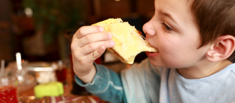 Kind eet stuk pizza met gesmolten kaas in restaurant