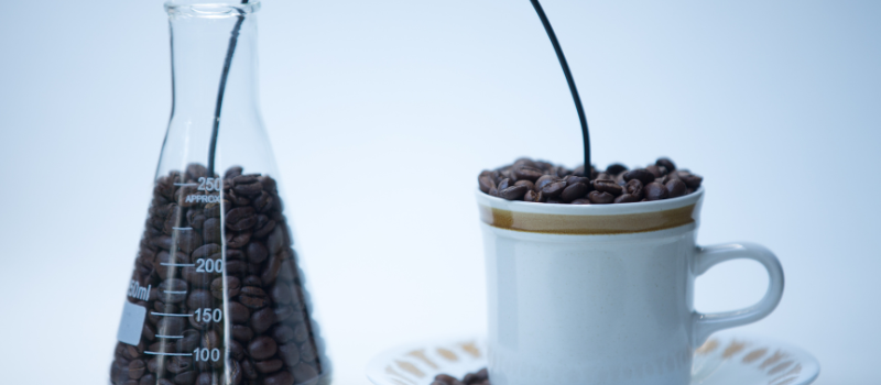 Koffiebonen in een glazen maatbeker en een witte koffiekop.