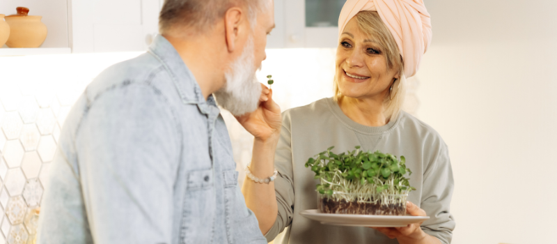 Oudere vrouw biedt man verse microgreens aan in de keuken.