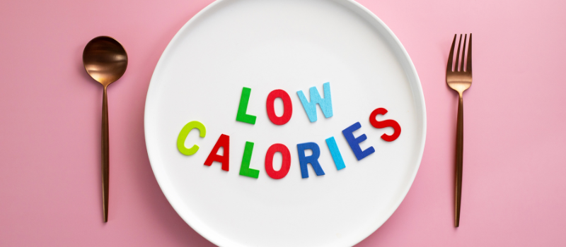 Bord met kleurrijke letters “low calories” tussen bestek op roze achtergrond