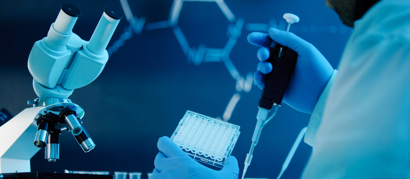 Onderzoeker met pipet in lab naast microscoop en monsterplaat