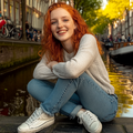 Lachende jonge vrouw met rood haar zit ontspannen bij een gracht, symbool voor positieve energie en balans.