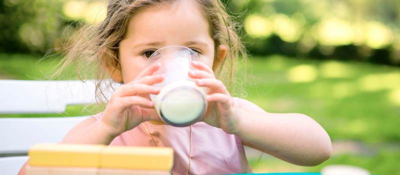 Klein meisje aan tafel drinkt een glas melk in een groene omgeving