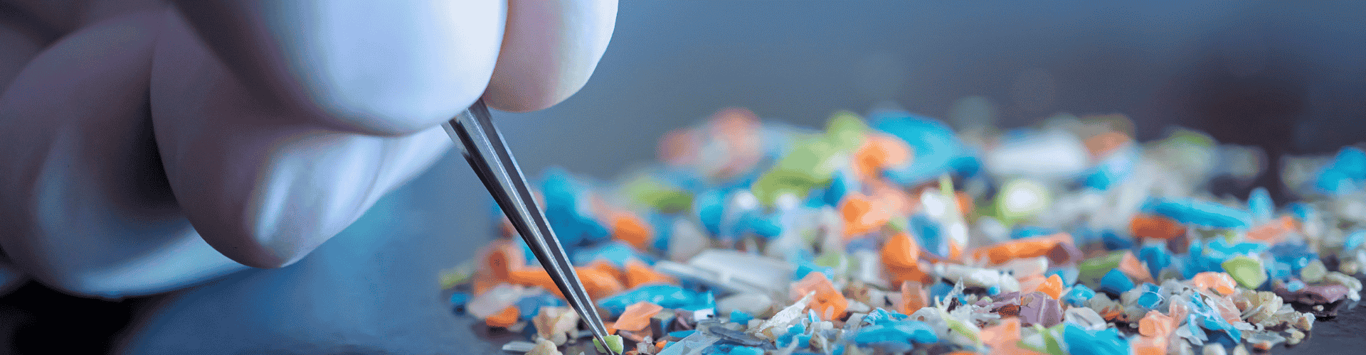 Hand met pincet onderzoekt kleurrijke microplastics op tafel