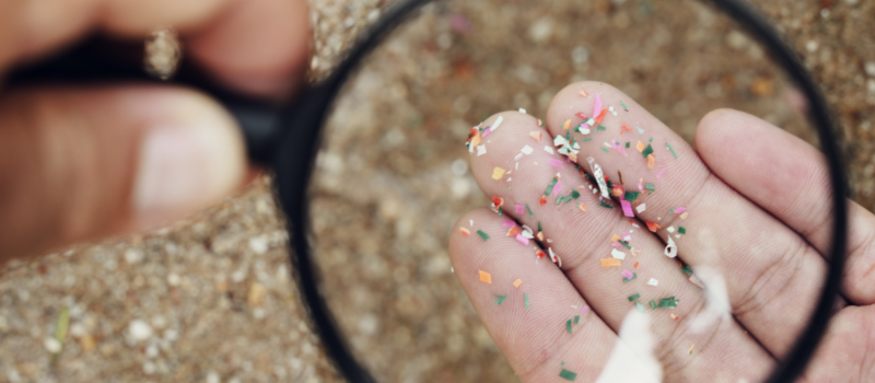 Hand met microplastics onder vergrootglas boven zand