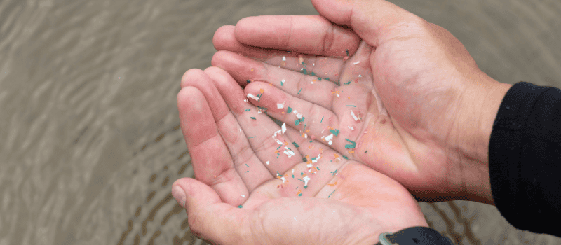 Handen gevuld met water en zichtbare microplastics, illustratie van vervuiling door microplastics in water