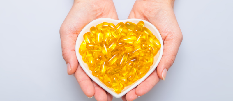 Handen houden hartvormig bakje met gele omega 3 capsules vast