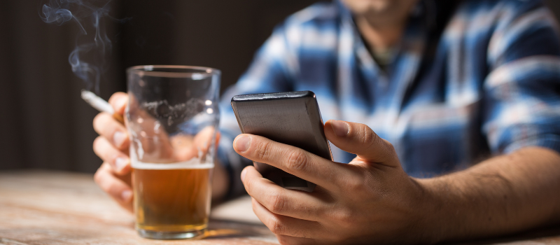 Man met bierglas, sigaret en smartphone in de hand