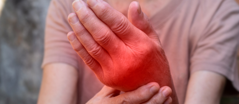 Rode gezwollen hand vastgehouden door oudere persoon, ontsteking, pijn