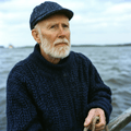 Oudere man met baard en marineblauwe trui staart over het water, symbool voor rust en hormonale balans