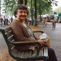 Glimlachende oudere vrouw zit op een bankje met een zak verse producten, symbool voor gezonde dagelijkse voeding.