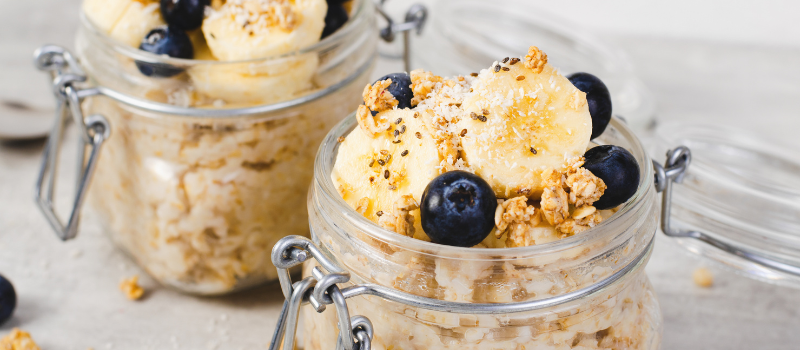 Glazen potjes met overnight oats, banaan, blauwe bessen en granola.