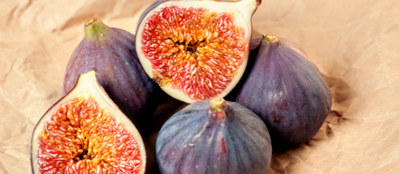 Drie paarse vijgen en twee gehalveerde vijgen op kraftpapier, vers gezond fruit