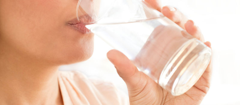 Persoon drinkt een glas water, focus op hydratatie en gezonde levensstijl.