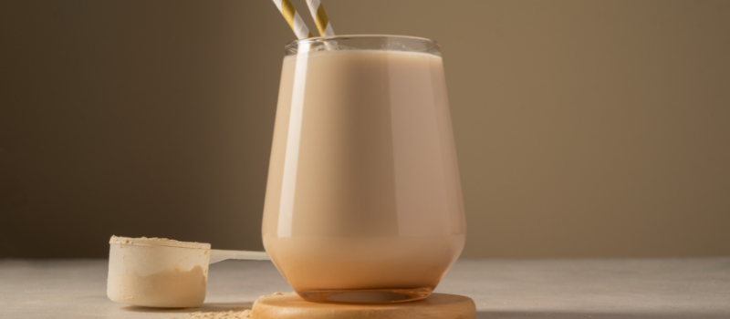 Glas met een proteïneshake en twee rietjes naast een schepje poeder op een tafel.