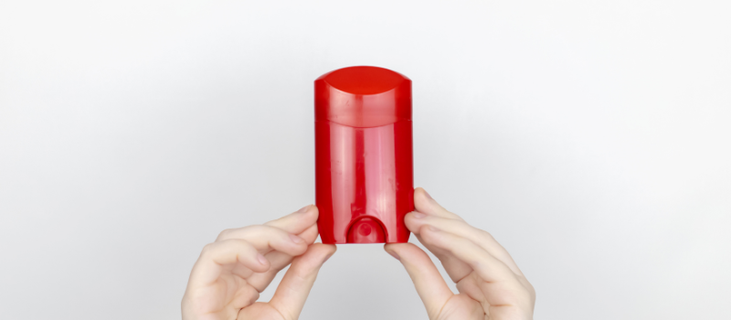 Handen houden een rode deodorantstick tegen witte achtergrond