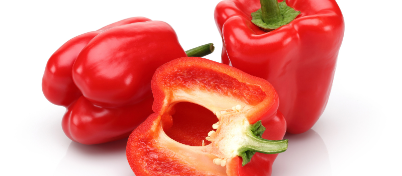 Drie rode paprika’s, waarvan één doormidden gesneden, op witte achtergrond