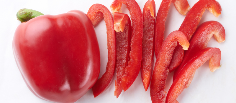 Rode paprika in plakjes gesneden op witte ondergrond, verse groente