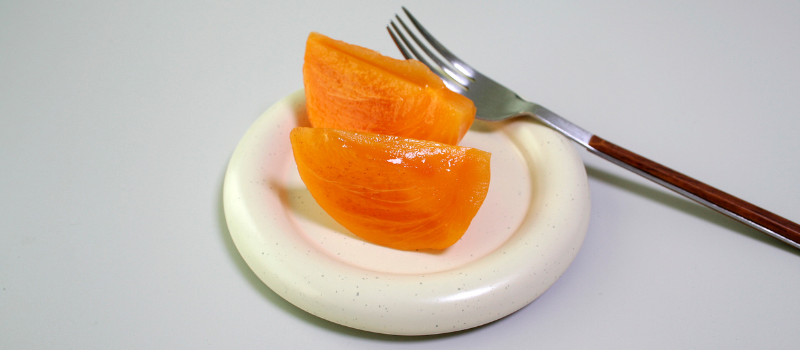 Twee schijfjes oranje fruit op een klein bord met vork, gezonde snack.