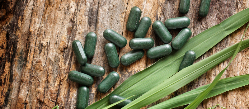 Spirulina-tabletten met bladeren op een houten achtergrond, een natuurlijke supplementoptie.