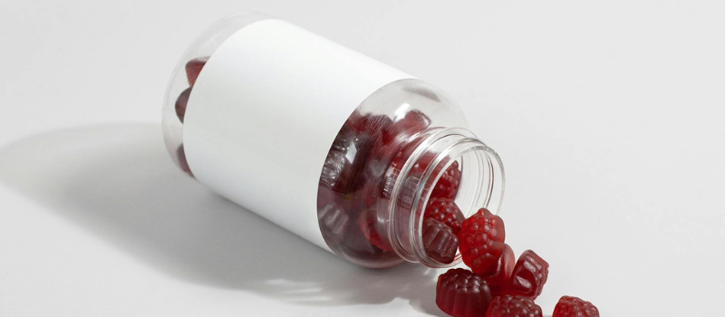Open fles met rode gummiesupplementen op witte ondergrond
