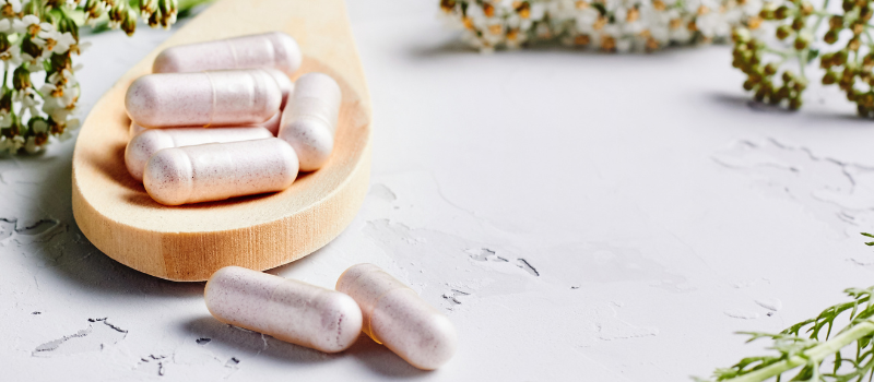 Capsules op houten lepel met kruiden op achtergrond, natuurlijk supplement