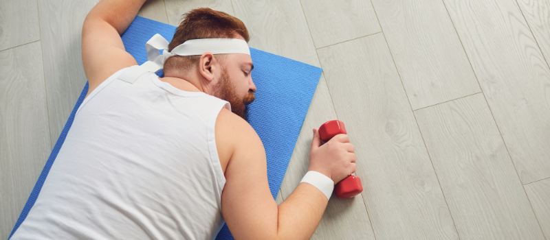 Vermoeide man in sportkleding slapend op yogamat met gewicht