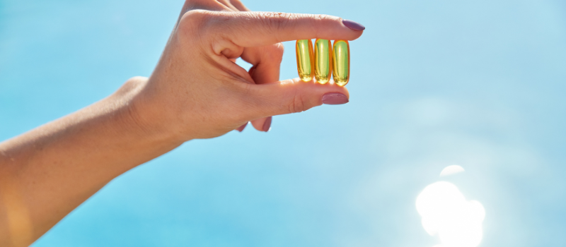 Hand houdt vitamine D capsules vast met blauwe lucht op achtergrond
