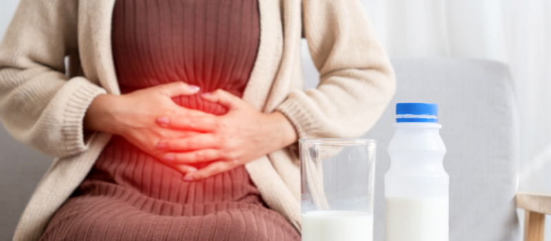 Vrouw met buikpijn en glas melk, mogelijk lactose-intolerantie