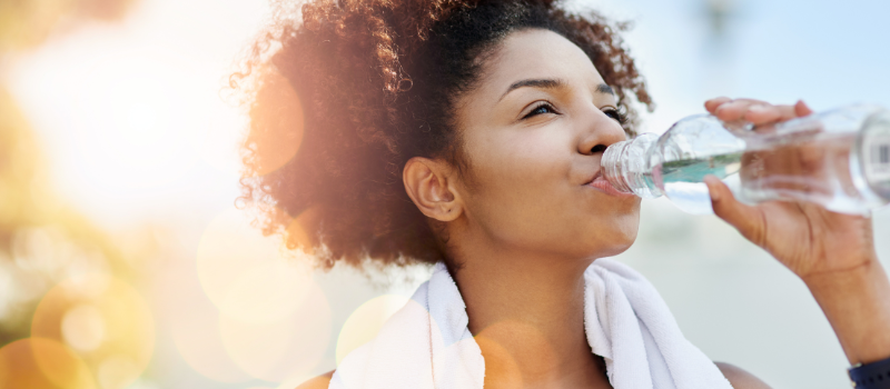 Vrouw drinkt een fles water in de zon na het sporten.