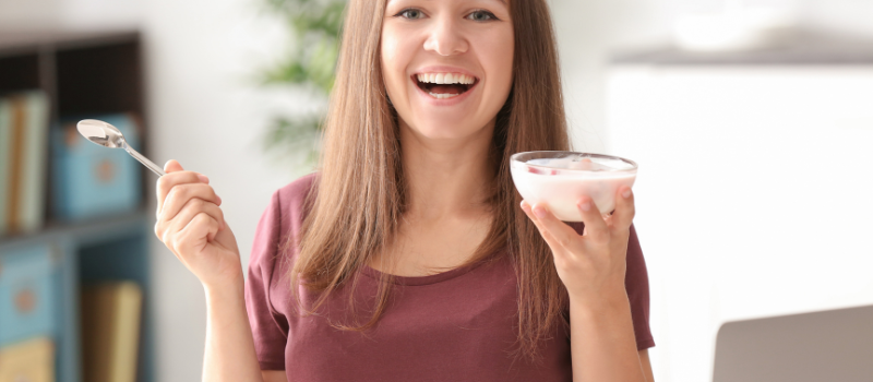 Vrouw lacht terwijl ze een kom yoghurt eet, zittend aan tafel.