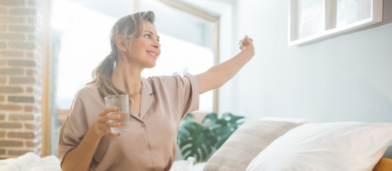 Vrouw met glas water geniet van de ochtendzon in slaapkamer