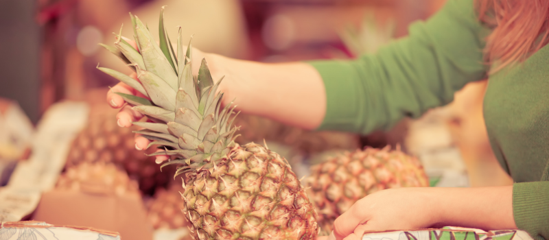 Vrouw kiest verse ananas op marktkraam, tropisch fruit kopen