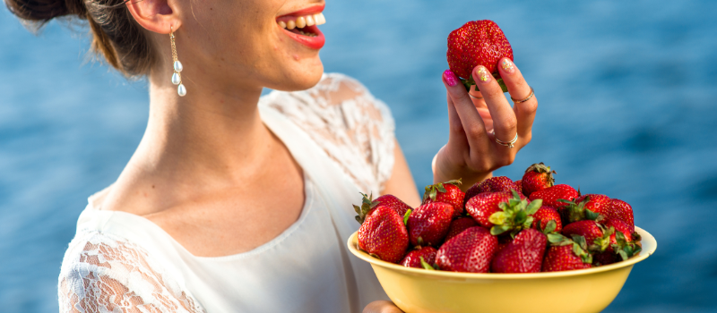 Vrouw houdt kom verse aardbeien vast bij water, zomerse sfeer
