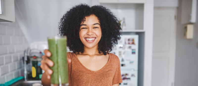 Lachende vrouw in de keuken met een groene smoothie, gezond en energiek.